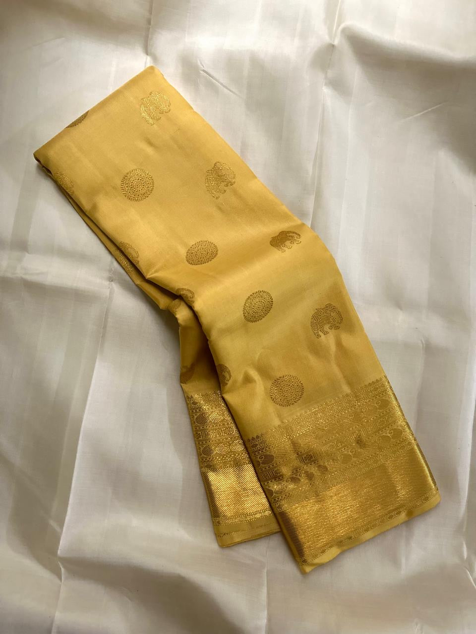 Close folded view showing alternating gold zari buttas across the Butter Yellow silk body