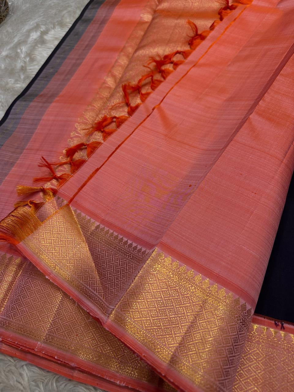 Folded pure Kanchipuram silk saree in purple black tones showing silk texture and shimmering zari border detail.