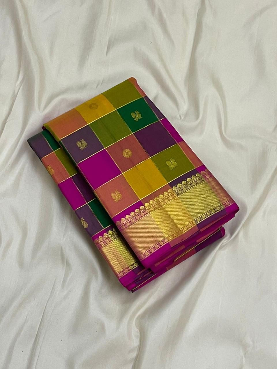 Folded Pure Kanchipuram silk saree with multicolor checks and zari woven gold border on white fabric background.