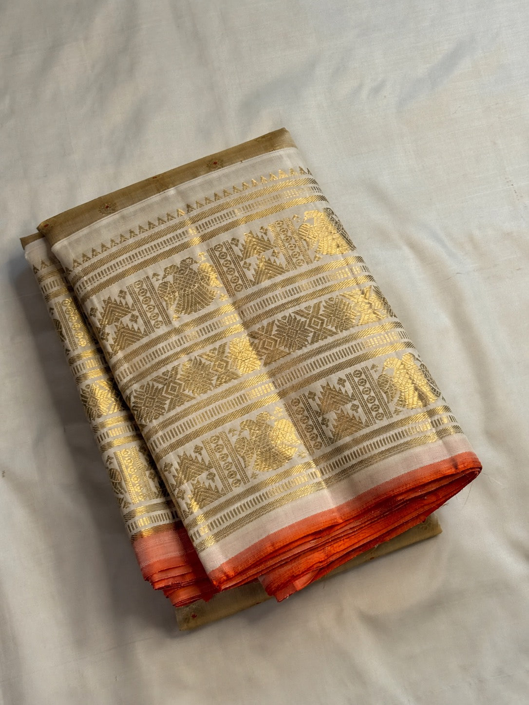 Pale gold handwoven Pure Silk Kanjeevaram Butta saree with orange Meenakari Kamalam motifs and coral-orange selvedge, folded silk detail