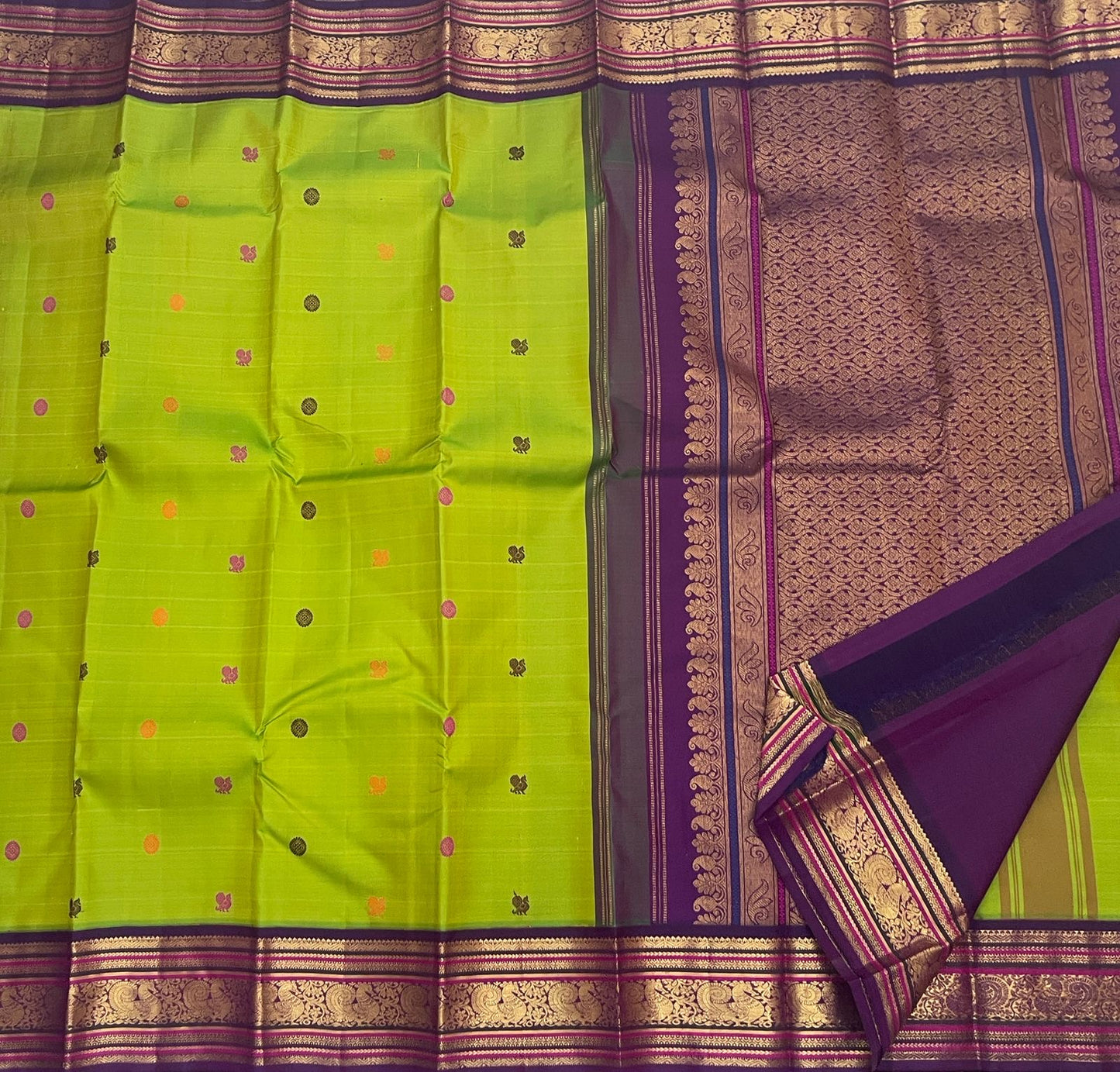 Parrot Green Kanchipuram Korvai saree showing Rani Pink and Orange silk-thread buttas with detailed gold Mayil border.