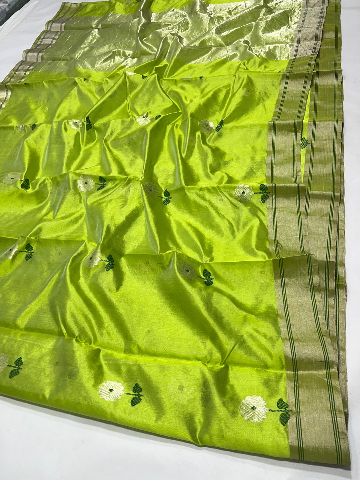 Close-up of white floral buttas and dark green leaves on a luminous parrot green Chanderi silk saree.