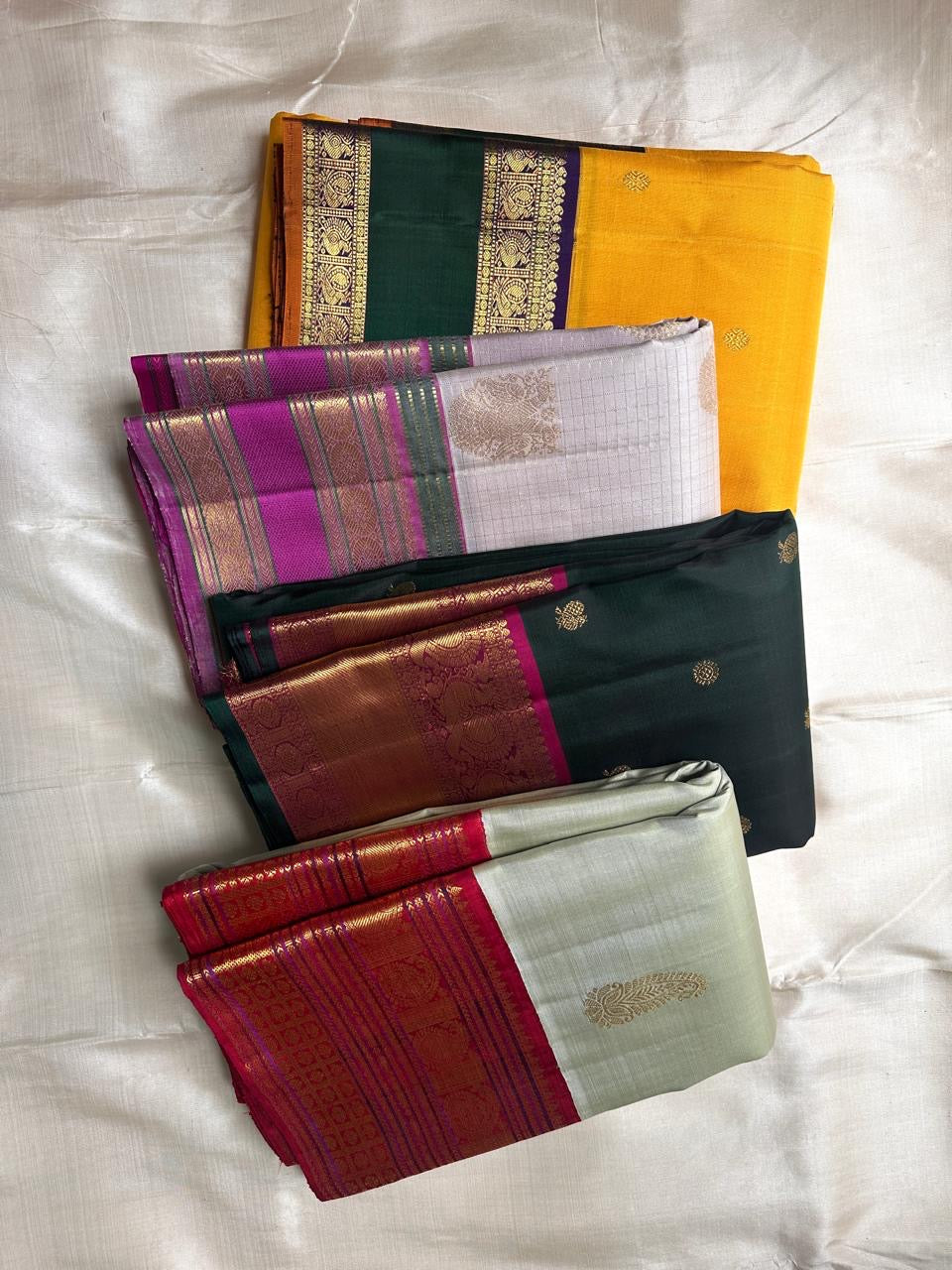 Stacked silk sarees showing sage green saree with maroon zari woven border and gold paisley motif
