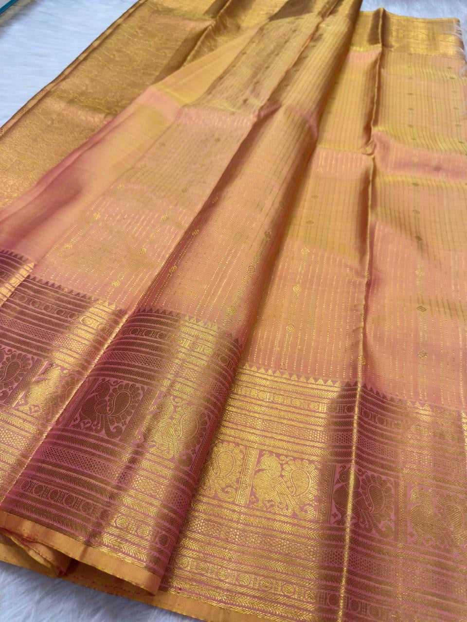 Close view of small gold zari buttas woven across luminous peach gold pure silk saree.
