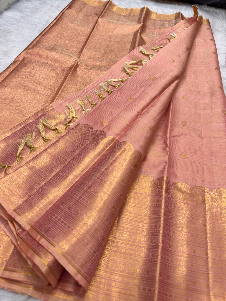 Folded Soft Peach Blush Pure Silk Kanchipuram Zari Kattam saree with gold buttas and ornate tonal zari border.