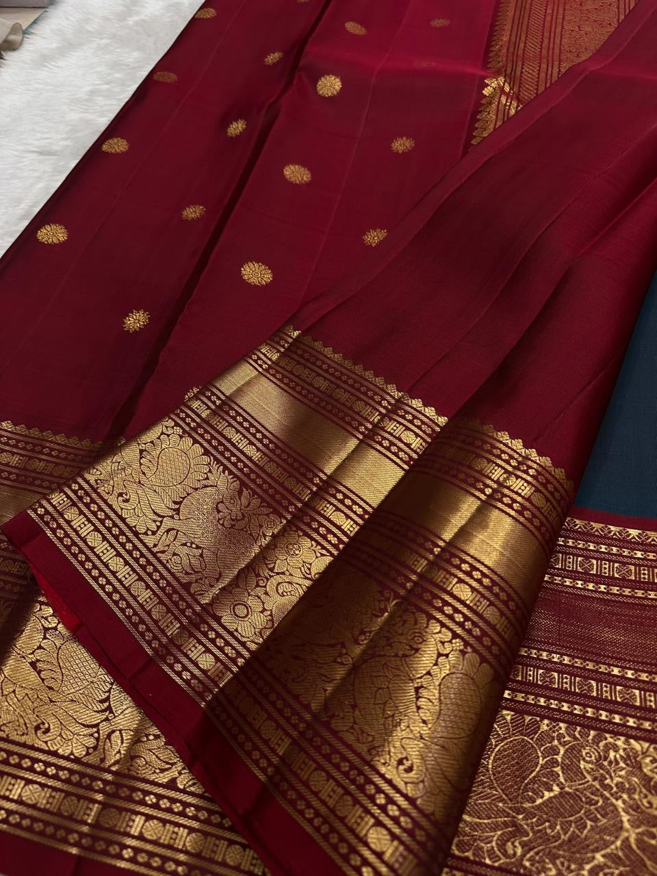Folded peacock blue Kanjeevaram pure silk saree showing shot colour body with Yaanai Ambari Butta and deep red border