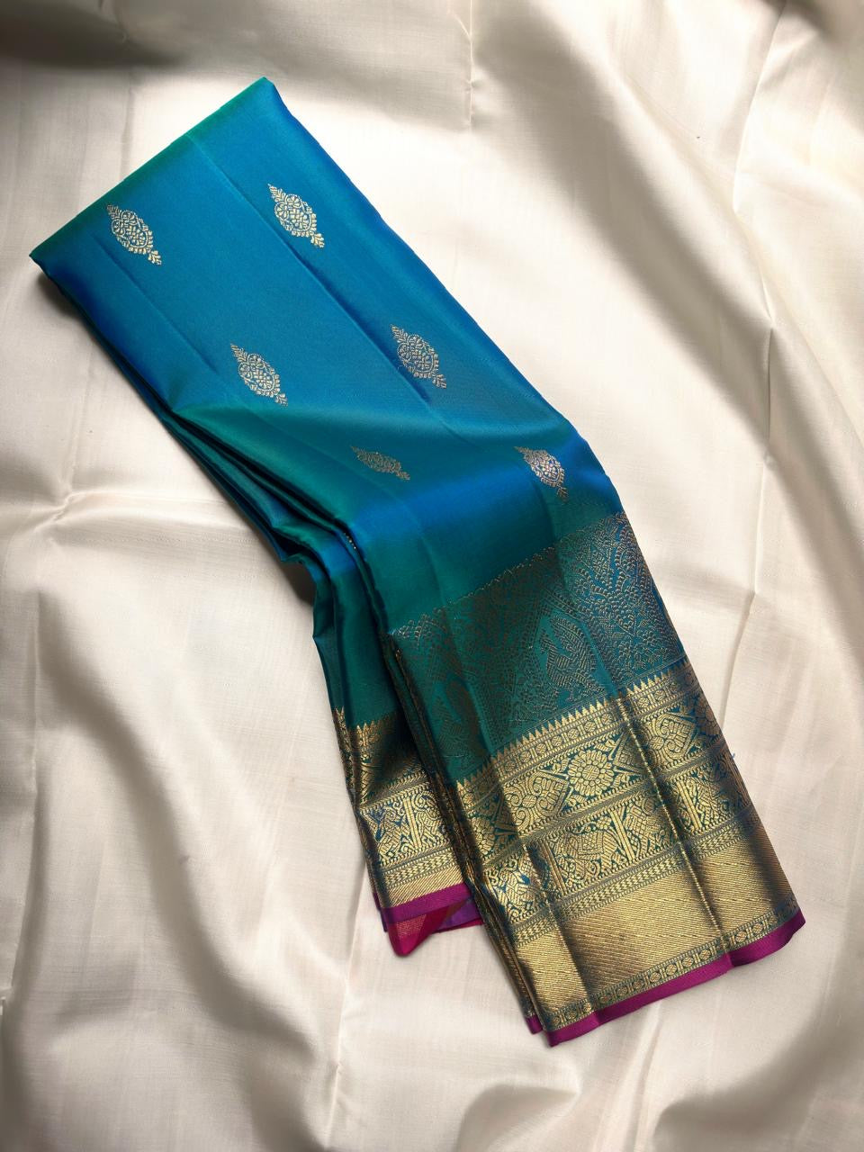 Peacock blue-green Kanjivaram saree with Rani-pink selvedge, gold zari Mayil motifs and temple-inspired Pettu