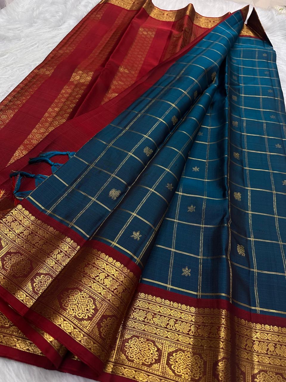 Fine gold Zari Kattam checks woven across the dark Peacock Teal pure silk body.