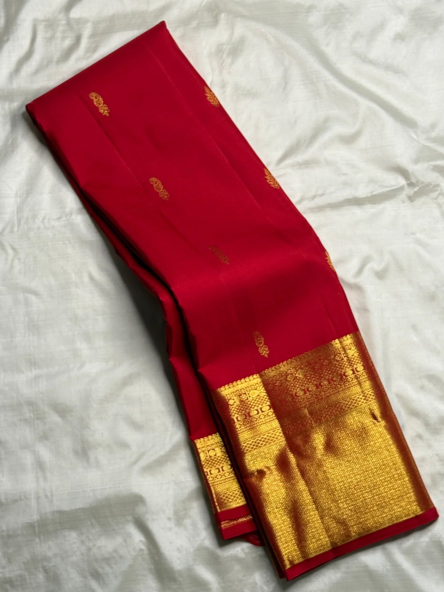 Folded Pillar-Box Red saree with compact gold buttas and broad geometric zari border.