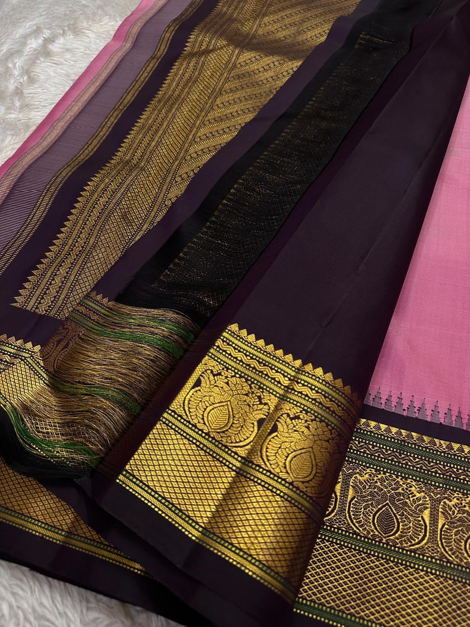 Close view of black zari pallu with dense gold zari patterns, green accent threads, and tassels on a pink silk saree