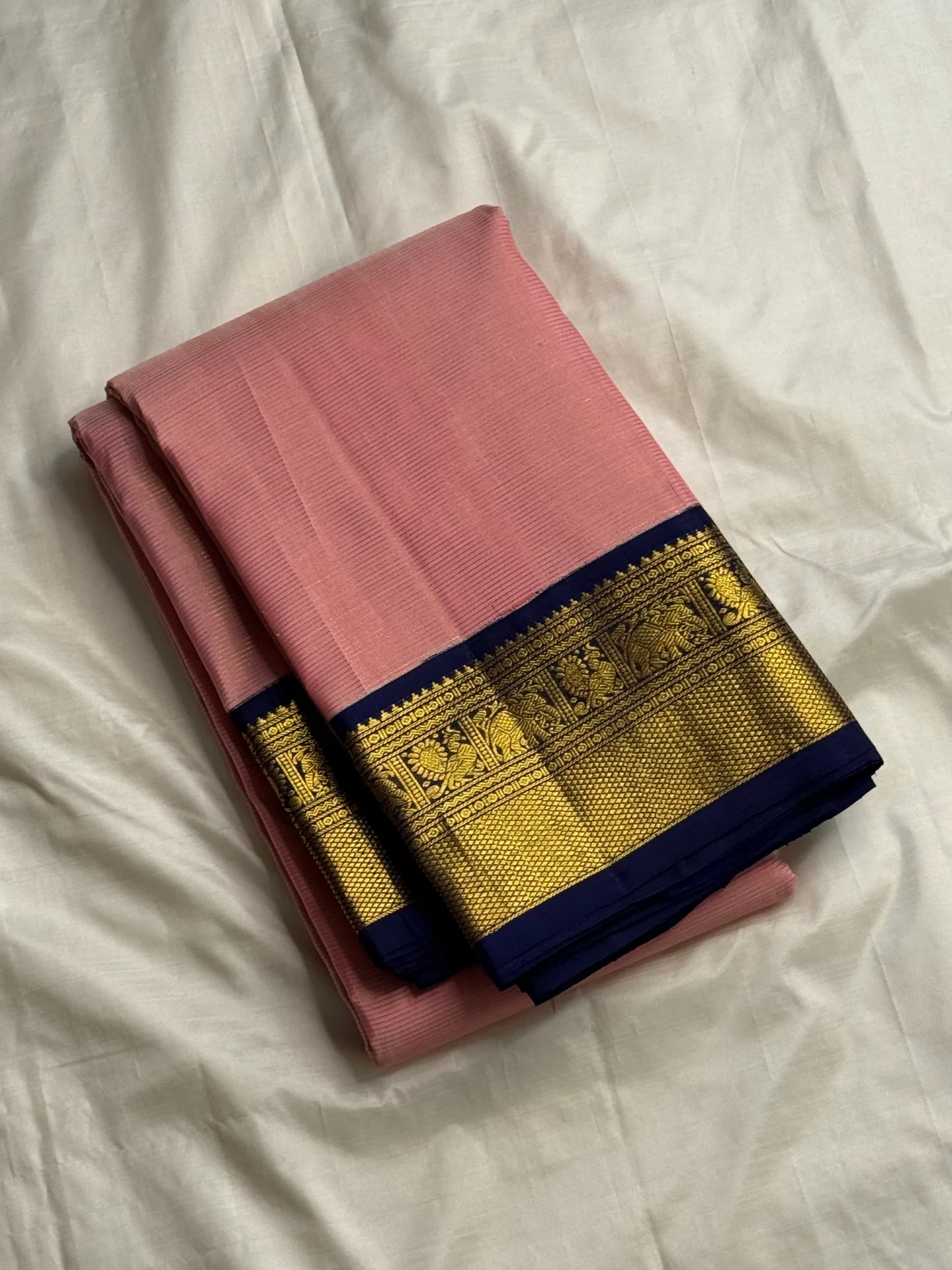Folded rose pink Kanchipuram silk saree with navy border and gold zari woven panel detailing