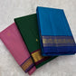 Three folded silk sarees on white fur background including rose pink with purple border, green, and ink blue with zari border