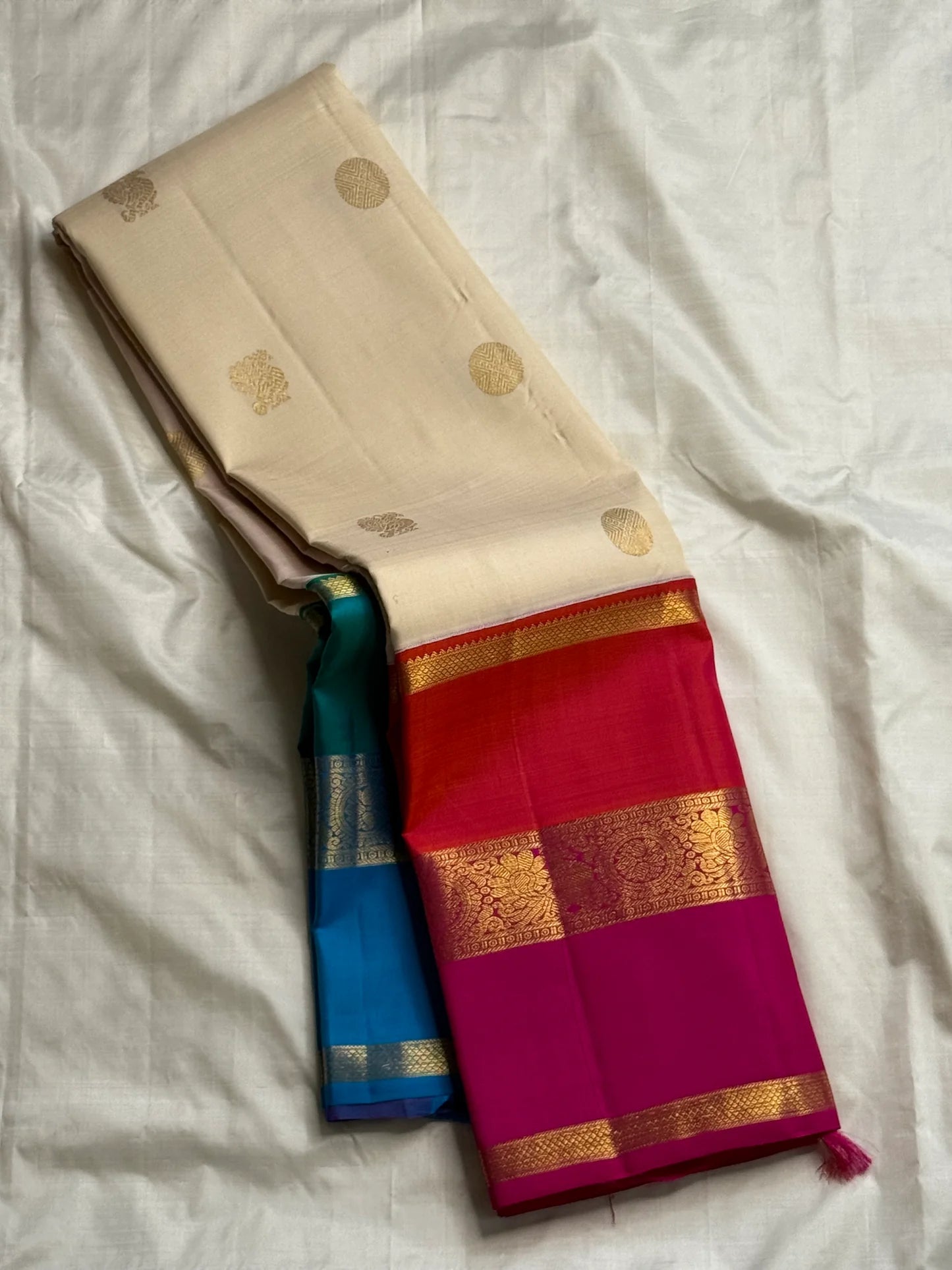 Hot pink bordered Kanchipuram silk saree fold showing wide zari woven panel and teal-blue contrast beneath.