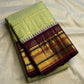 Pale pistachio-green body meeting the deep aubergine Korvai border with layered gold-zari registers.