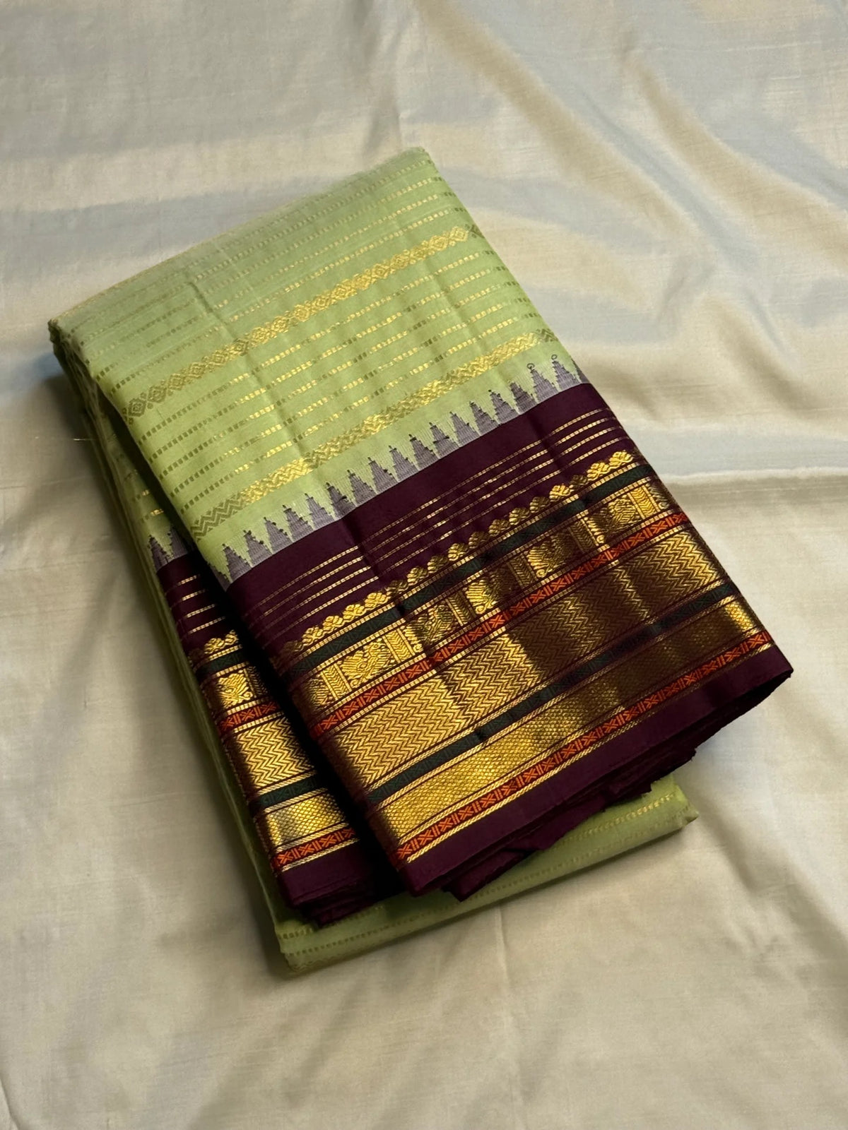 Pale pistachio-green body meeting the deep aubergine Korvai border with layered gold-zari registers.