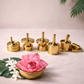 Set of five 2-inch pure brass oil wick holders arranged on a neutral surface with lotus flower and jasmine, traditional diya accessories for pooja and temple decor.