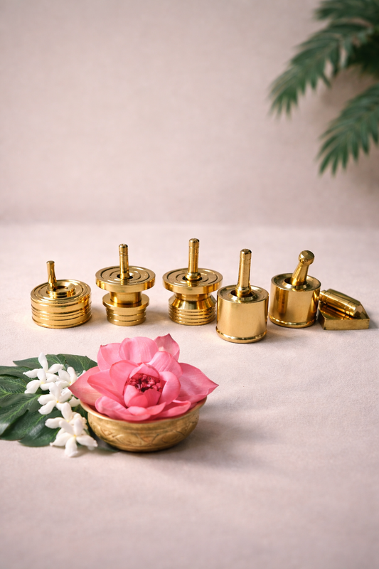 Set of five 2-inch pure brass oil wick holders arranged on a neutral surface with lotus flower and jasmine, traditional diya accessories for pooja and temple decor.