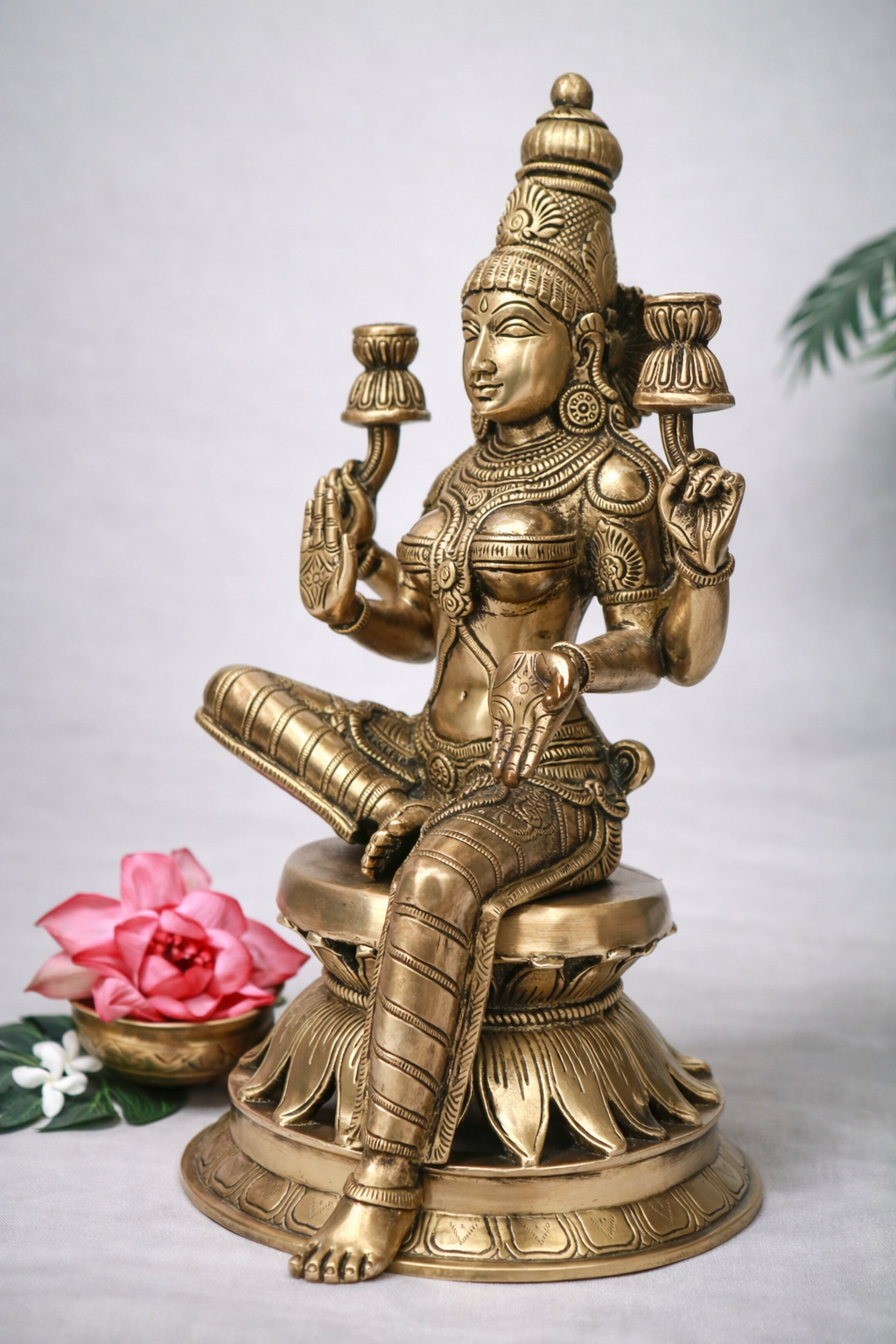 Front angled view of pure brass Lakshmi statue, 30 cm height, detailed crown, mudras and lotus pedestal, styled with pink lotus and jasmine flowers.