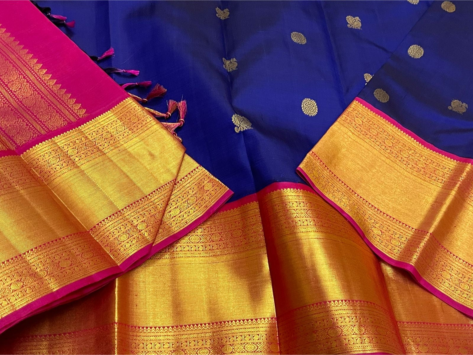 Close-up of blue saree body with gold zari buttas, gold zari border with pink edge, and visible tassels near the pallu.