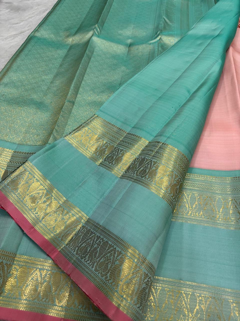 Blush rose Kanjivaram silk saree folded, showing peacock teal border contrast