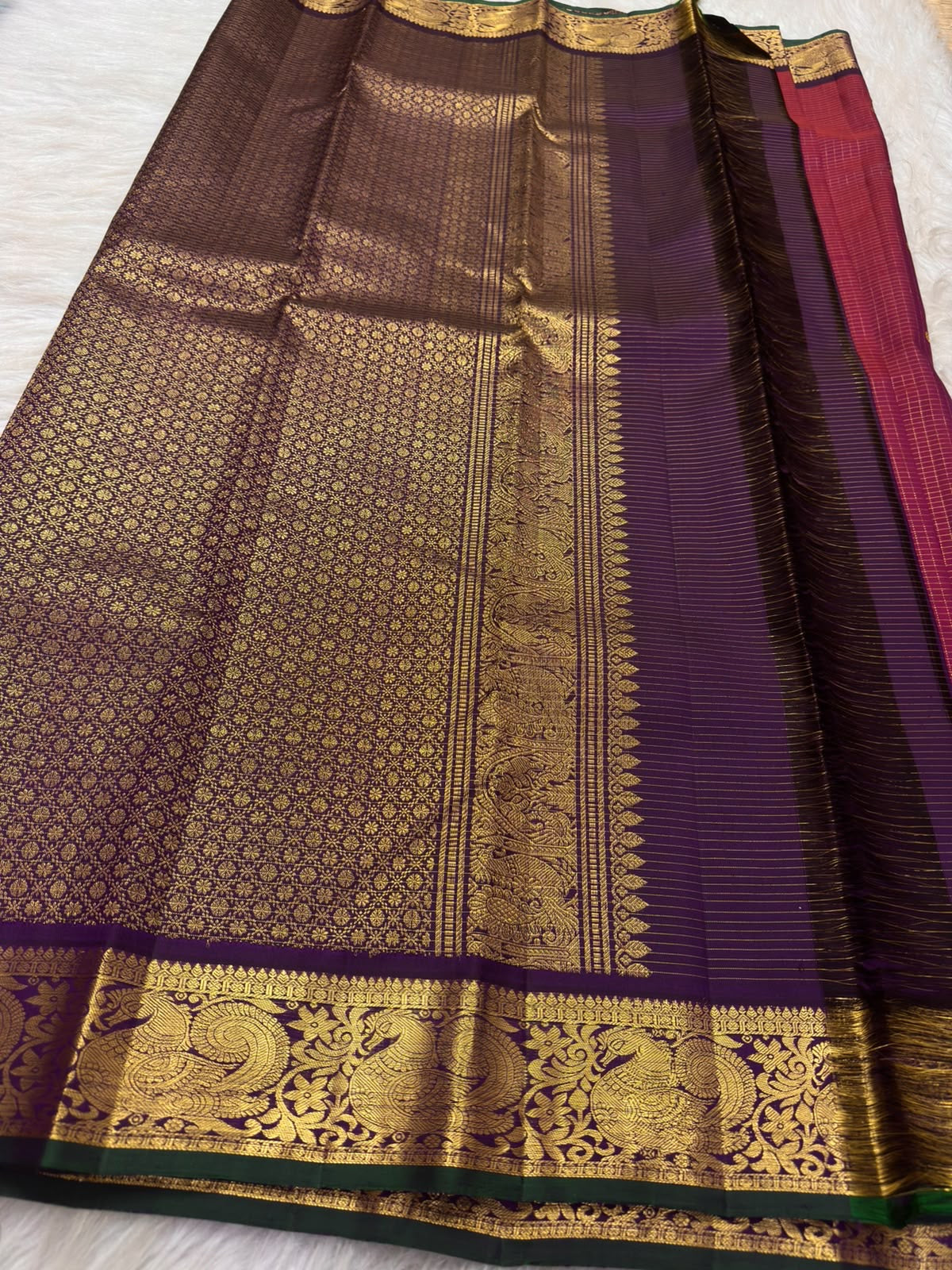 Raspberry red Kanchipuram silk saree folded, showing checked body, aubergine peacock border and pallu