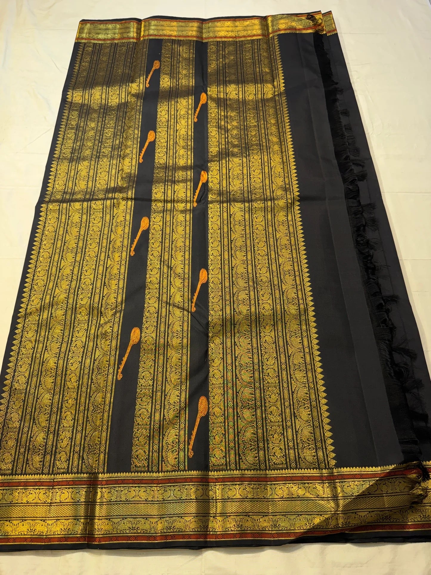 Black Kancheevaram silk saree with antique gold zari border and vermilion accents.