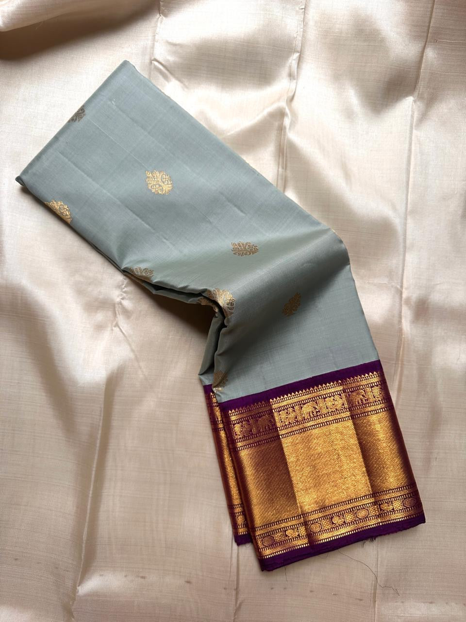 Dovetail grey Pure Kanchipuram Silk Saree showing gold buttas and wide purple zari border in a folded drape
