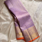 Lavender pure Kanchipuram silk saree draped to show gold zari border with orange edge on beige silk backdrop.