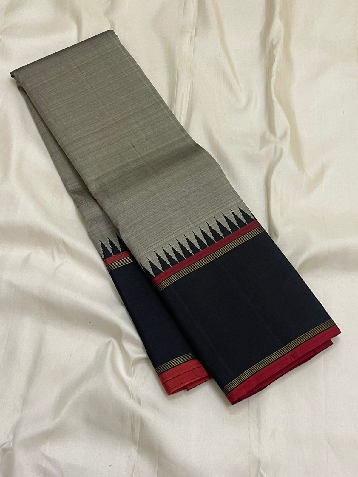 Folded grey Pure Kanchipuram silk saree showing black border with red selvedge and pillayar reku edge detailing.