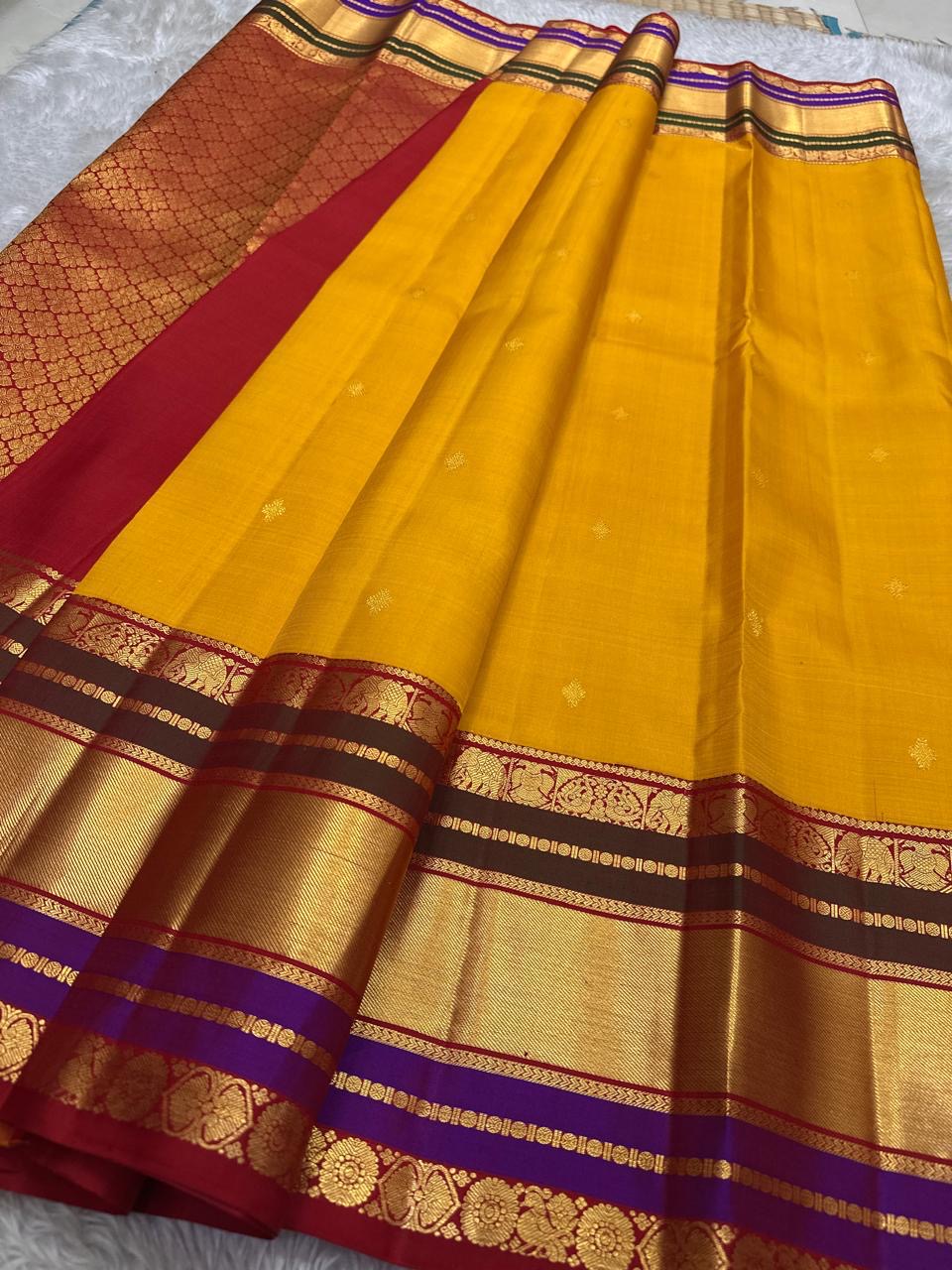 Full spread of mustard yellow Pure Kanchipuram Silk Saree with scattered buttas and wide zari border; pallu section visible at left.