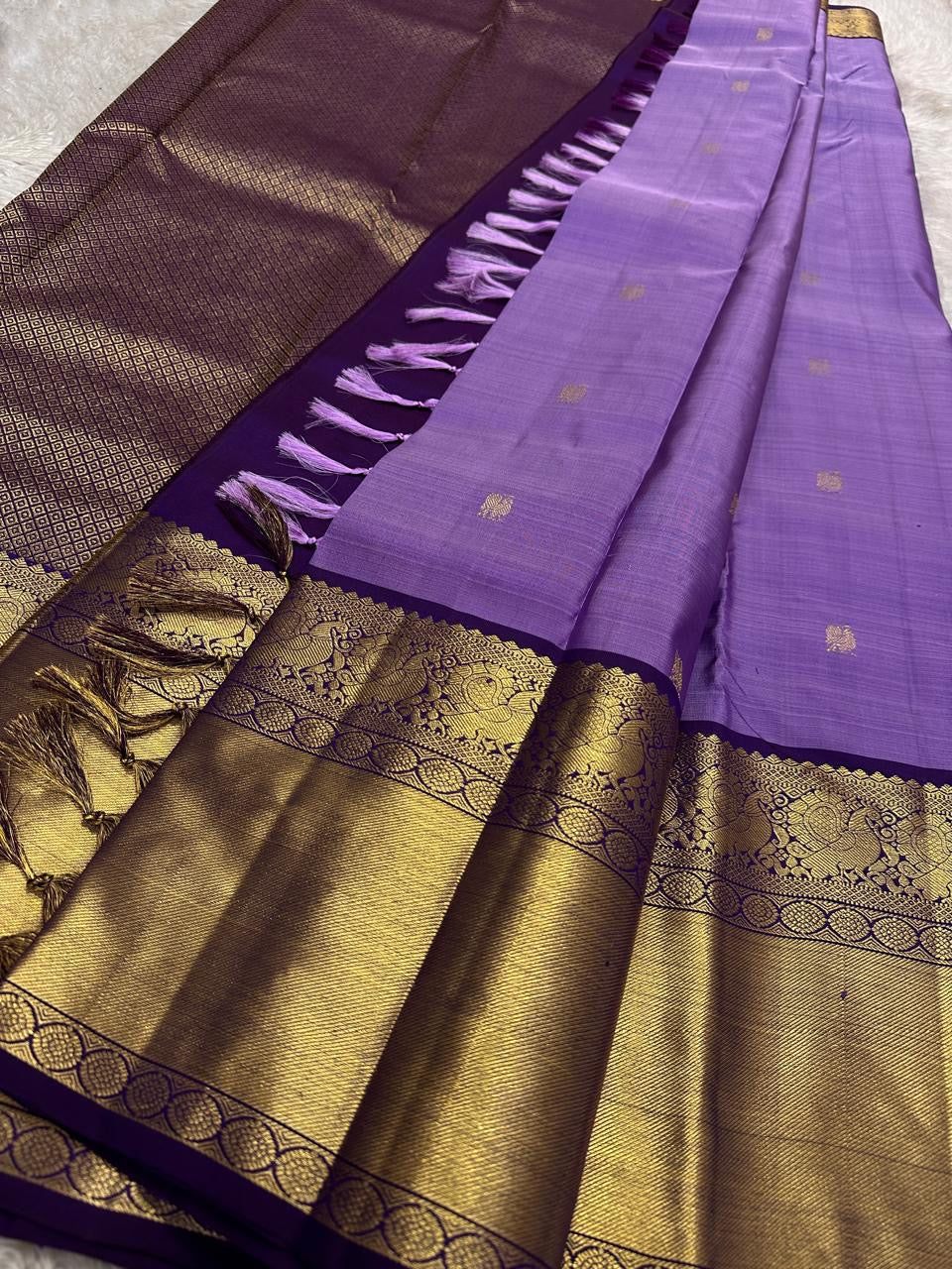 Purple Kanchipuram silk saree showing antique gold zari border detail and pallu tassels laid flat