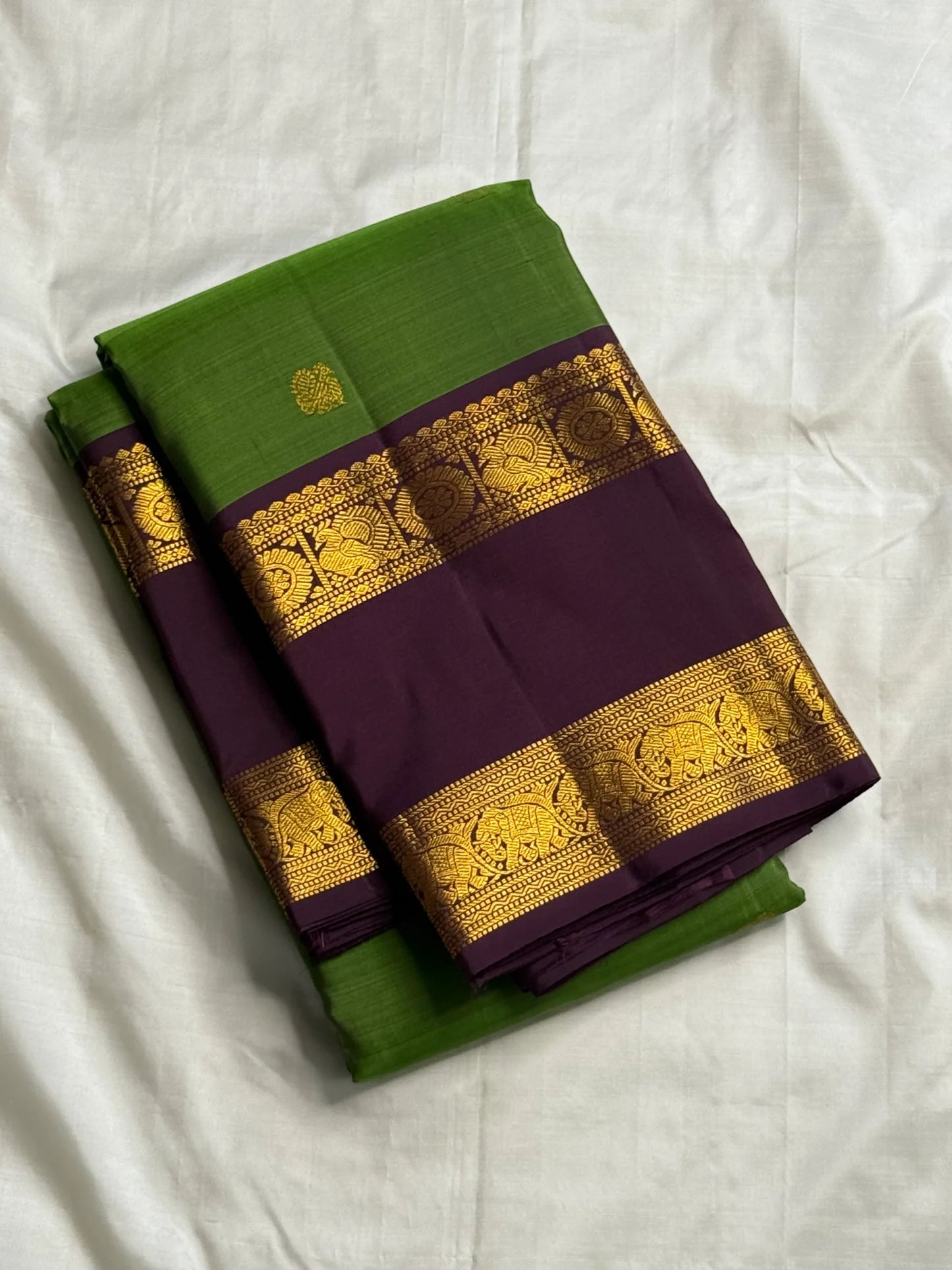 Folded green Pure Kanchipuram silk saree with small gold woven motifs and deep purple zari woven elephant border