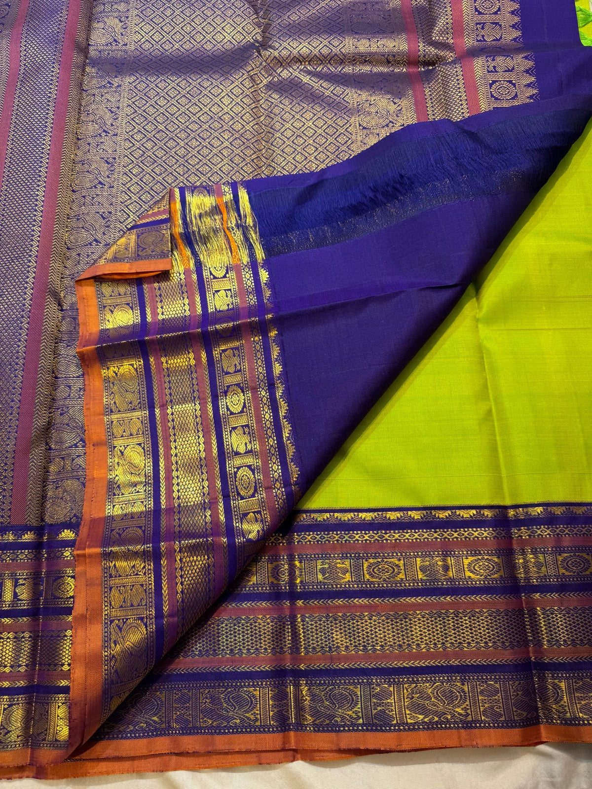 Full lime-green handwoven Kancheepuram silk saree with deep indigo-purple and gold zari border registers.
