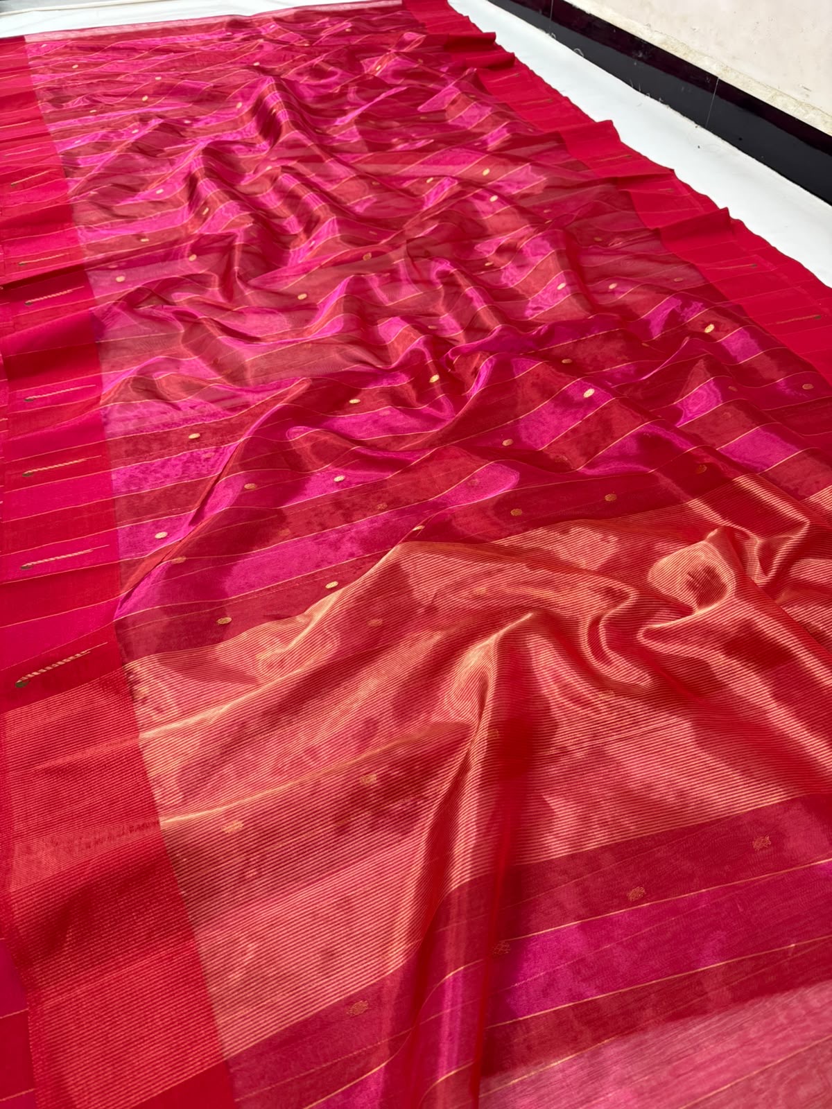 Folded Rani Pink handloom Tissue Silk Chanderi showing linear jari weaving, petite gold buttas and painted border accents