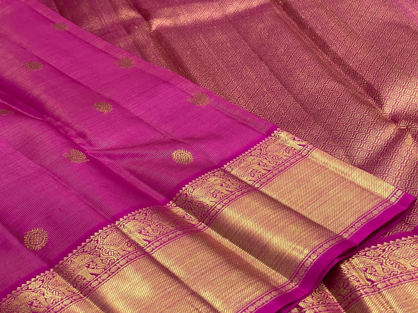 Dense gold zari pallu with repeating geometric field on saturated Rani Pink silk.