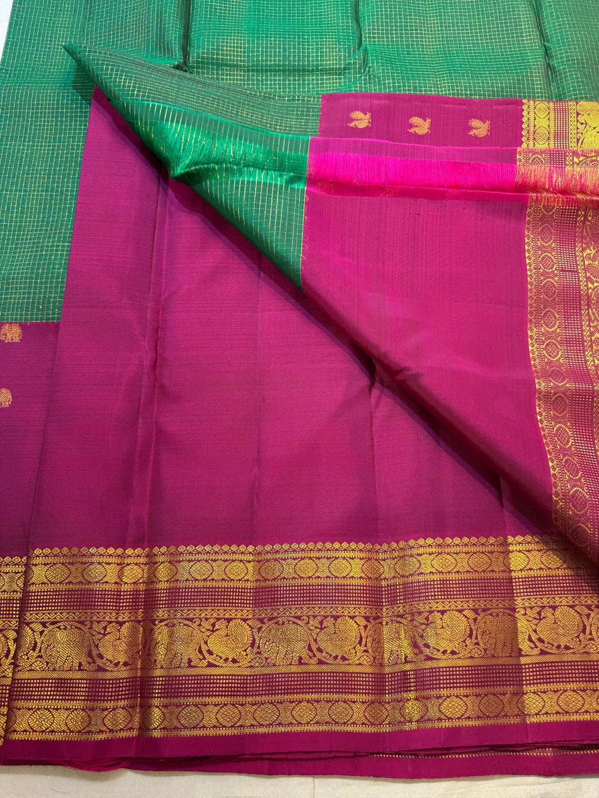 Rani Pink Korvai border with layered warm-gold zari on Emerald Green Kanchipuram saree.