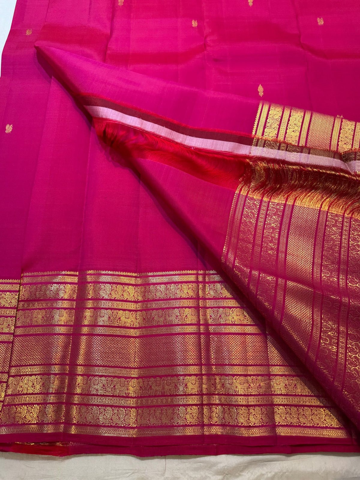 Bright raspberry pink Kanchipuram Varisaipet saree with handwoven antique-gold body motifs.