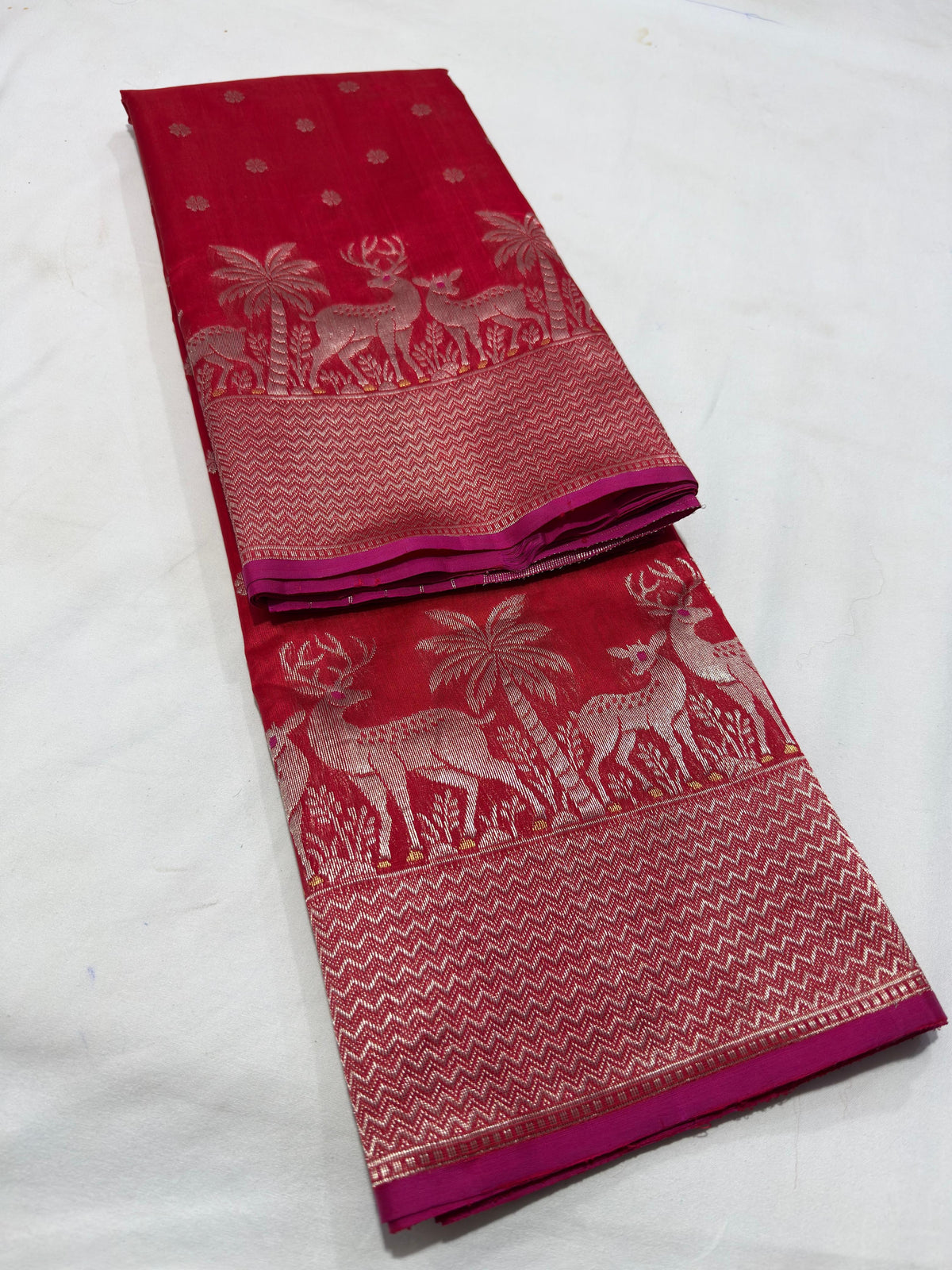 Folded red Chanderi silk saree showing deer and palm-tree zari border with chevron detailing