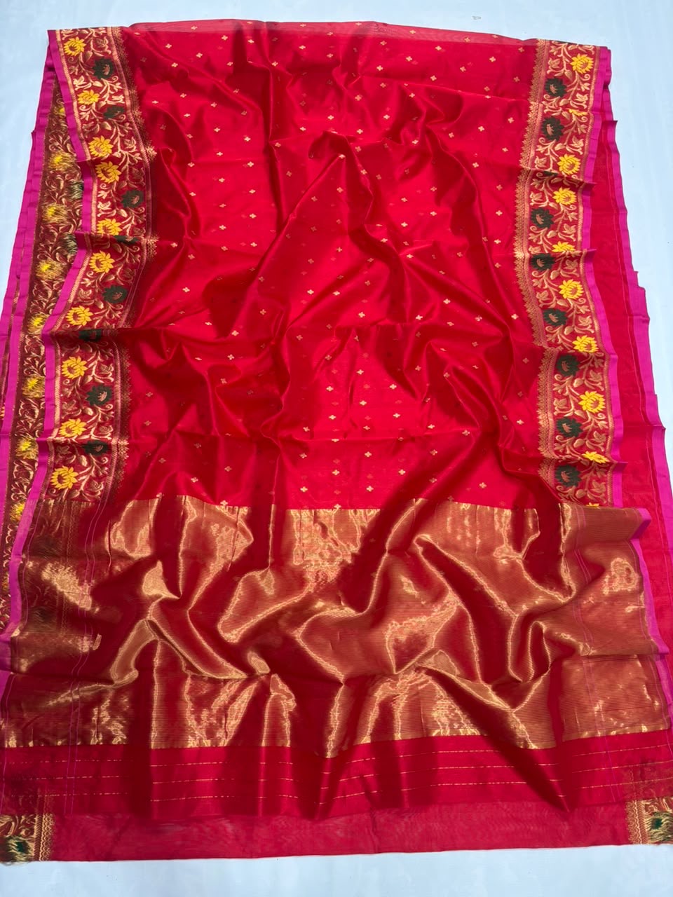 Folded red Pattu Silk Chanderi saree showing petite gold buttas and richly woven multicolour floral border