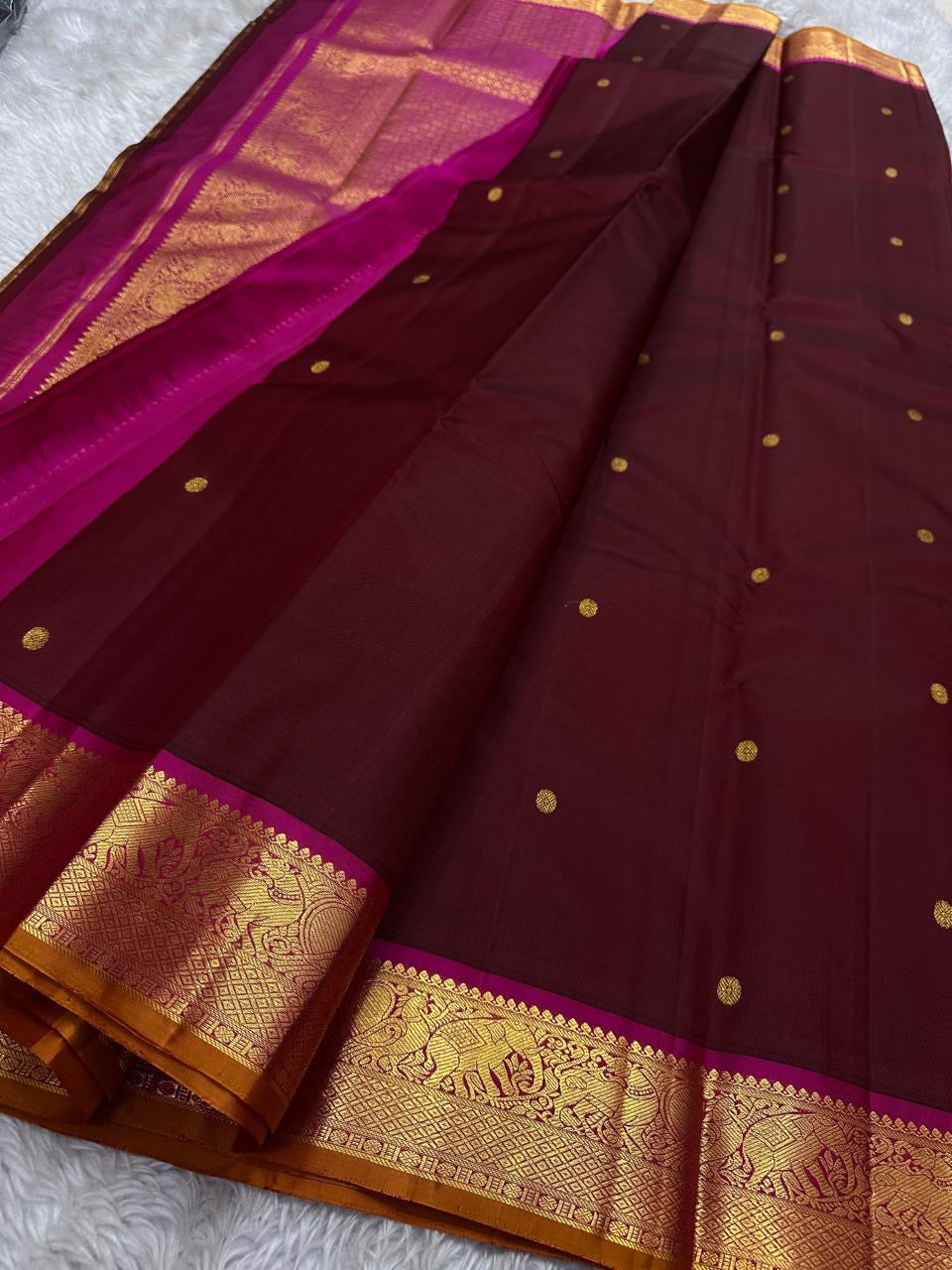Saree body in deep red with gold buttas and wide zari woven border beside magenta pallu.