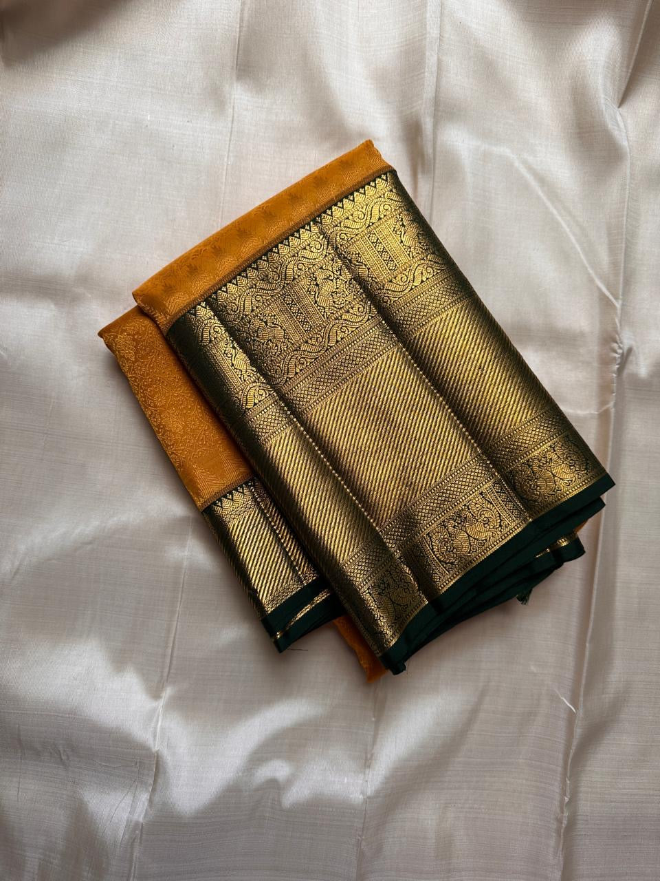Folded Pure Kanchipuram silk saree in mustard yellow with dark green and zari woven gold border.