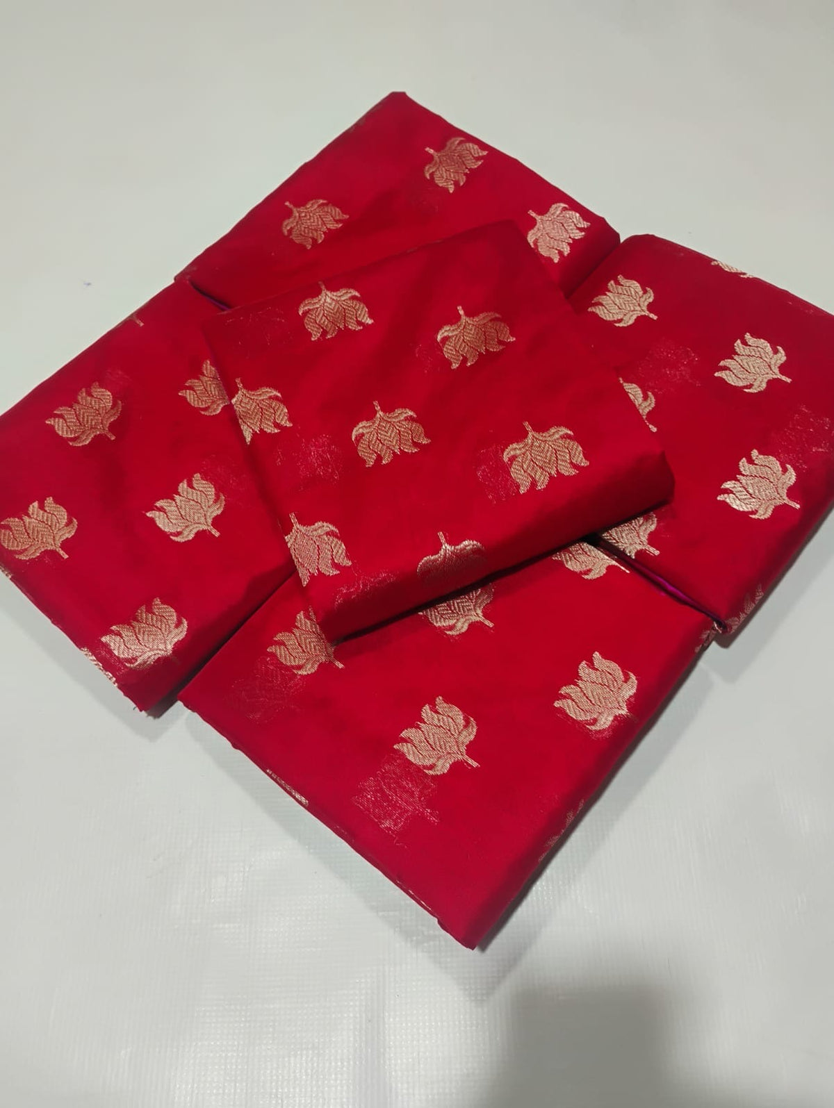 Folded red Pattu Silk Chanderi saree showing repeating gold-toned floral buttas.