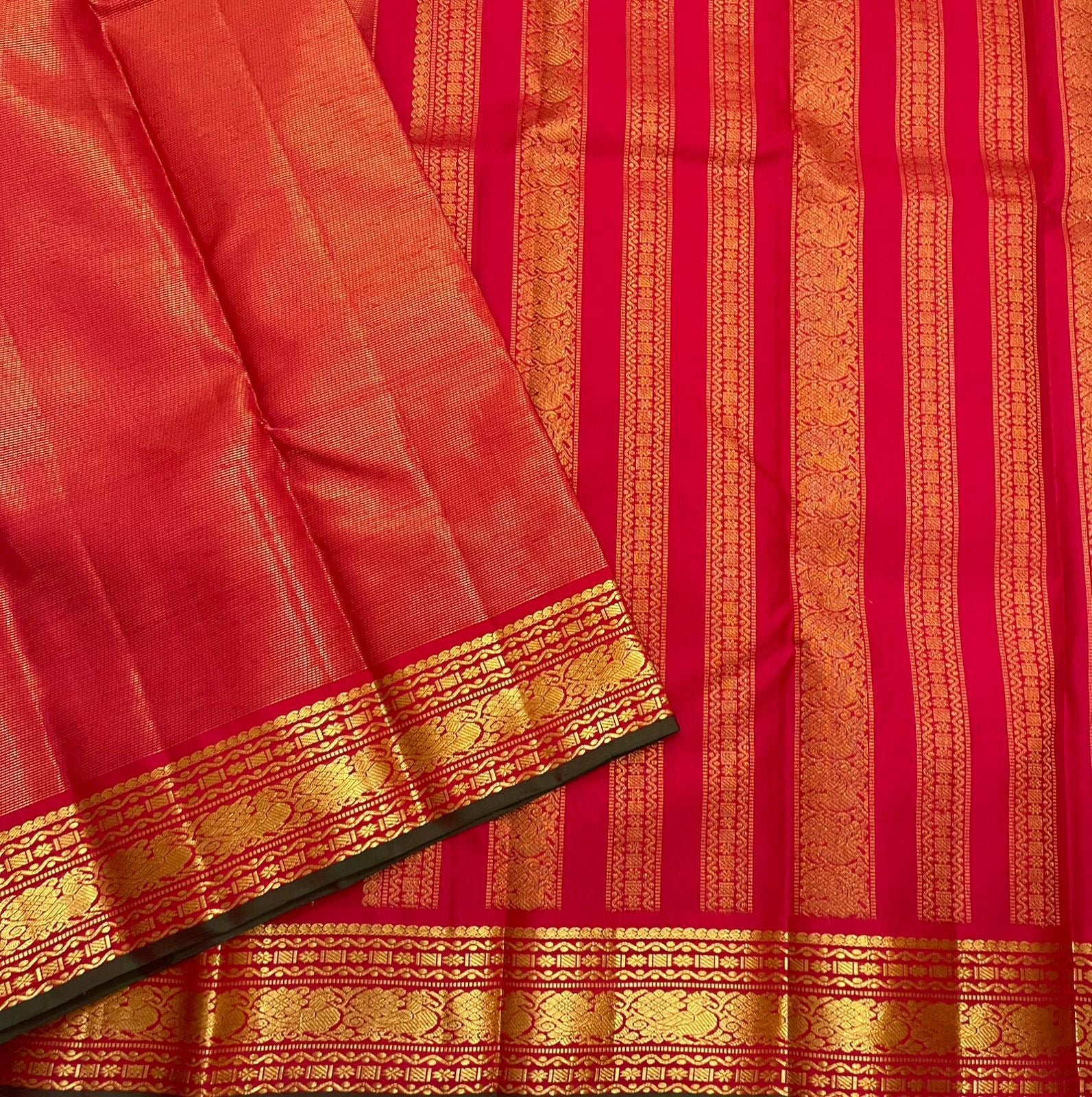 Close view of red silk saree border with gold zari pattern bands and forest green selvedge along the edge.
