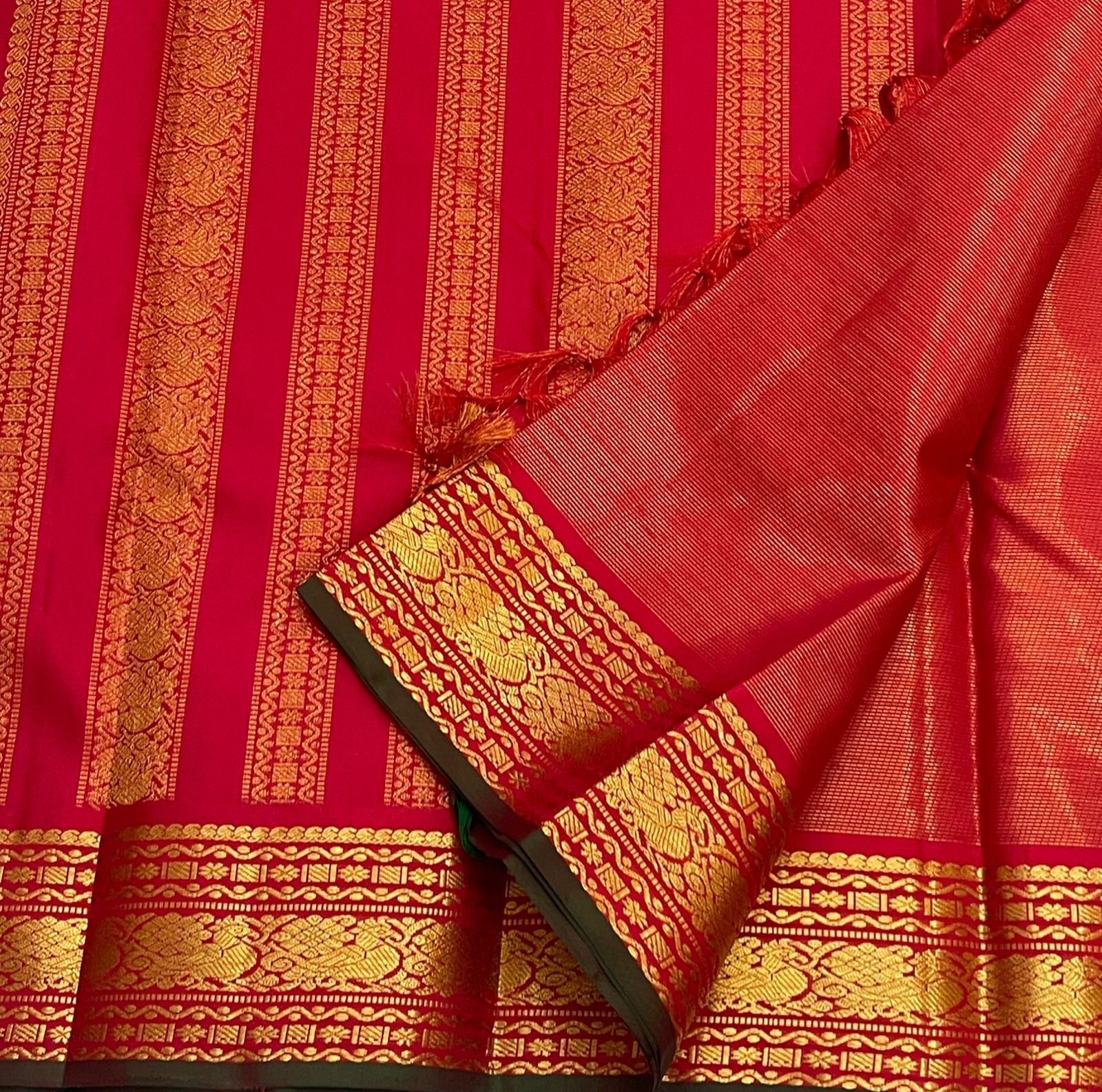 Red saree pallu with vertical gold zari stripes and tassels, showing woven border with forest green edging.