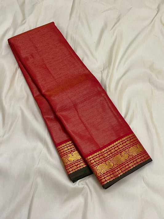 Long folded red Kanchipuram silk saree showing gold zari border panel and dark green selvedge on white sheet.