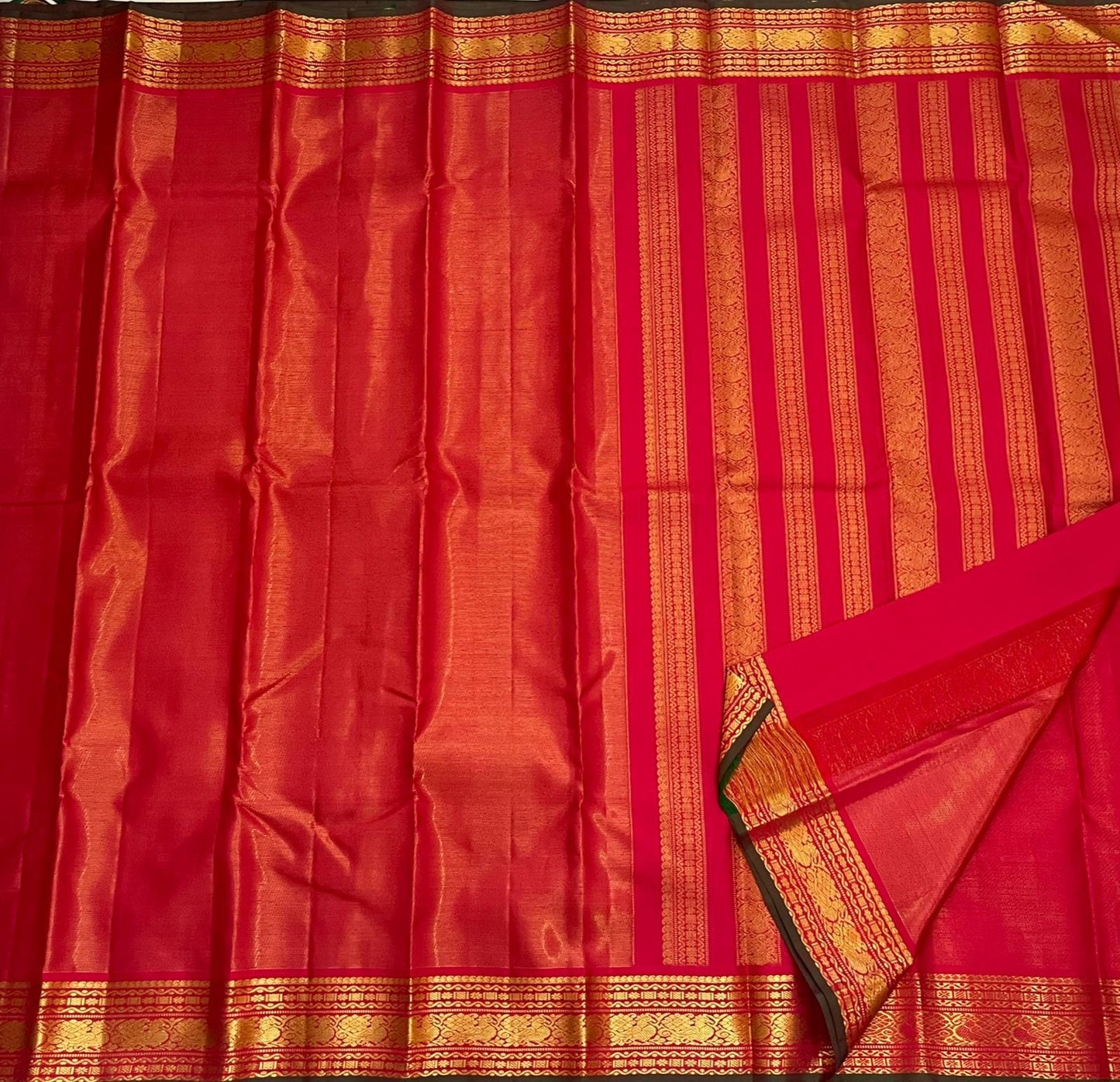 Full length red Kanchipuram silk saree laid flat with striped pallu and wide gold zari borders, available in the USA.