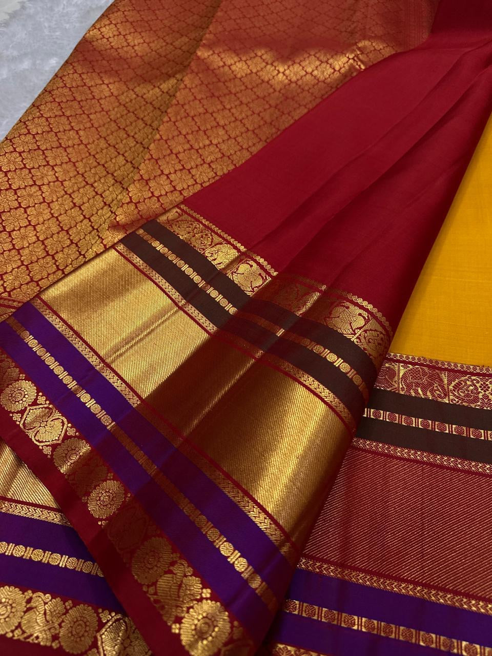 Close-up of red pallu with gold zari woven floral pattern and border bands in maroon, gold, and purple.