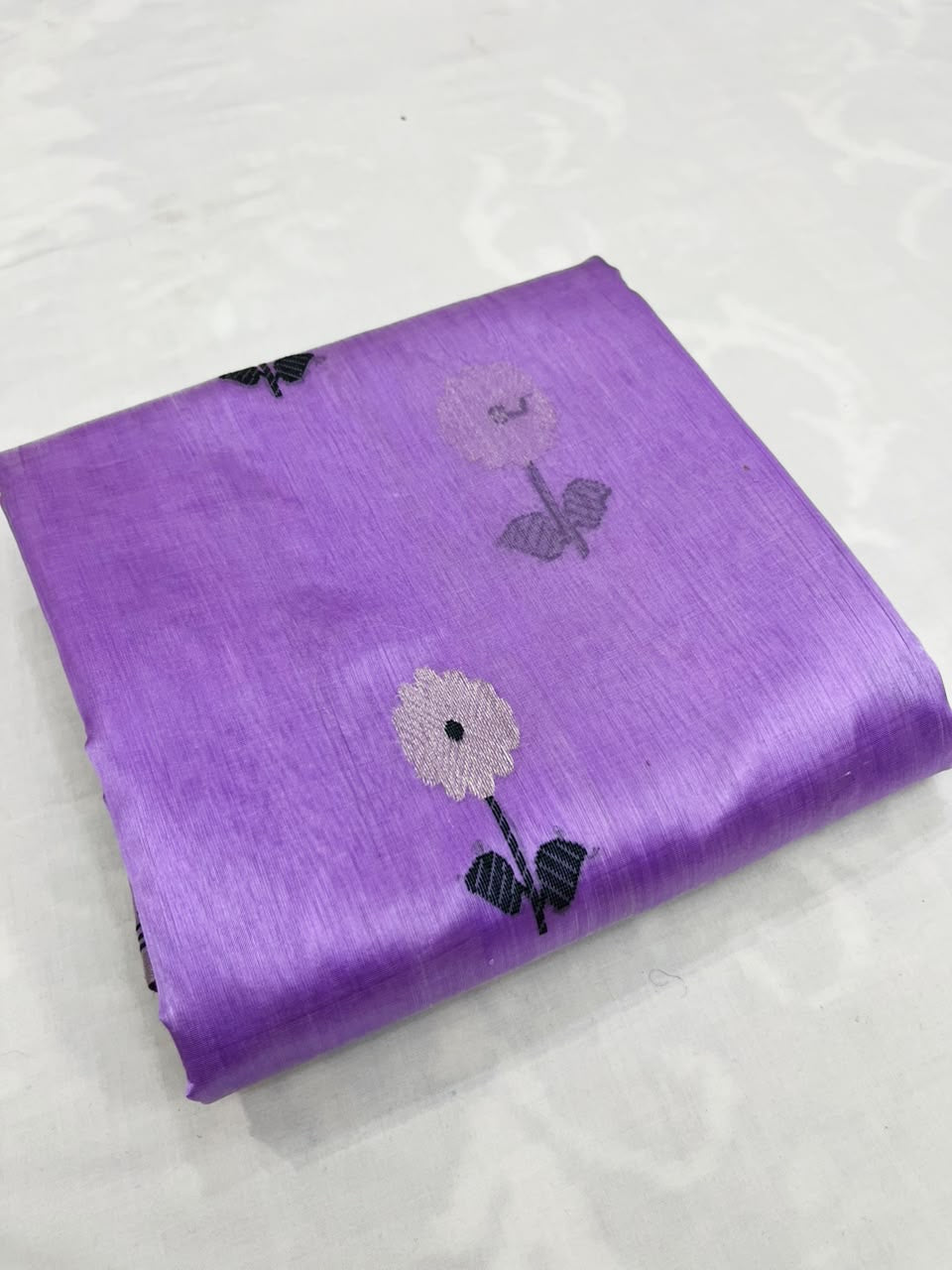 Folded lilac Chanderi Pattu silk saree with a close view of the white floral buti and dark leaf detail