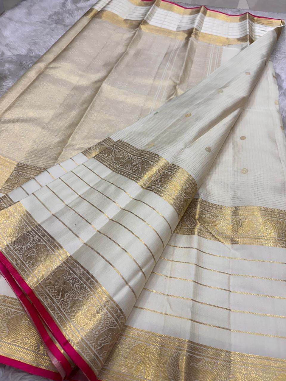 Narrow vivid rose-pink selvedge along the elaborate gold zari border of ivory silk.