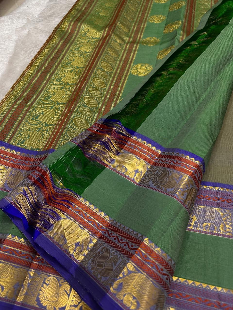 Moss Green Shot Silk pure silk Kanchipuram saree, border detail, showing muted olive-moss and sage green shot with golden undertones, brighter emerald pallu, deep cobalt-blue silk-thread accents, copper-rust bands and antique-gold zari